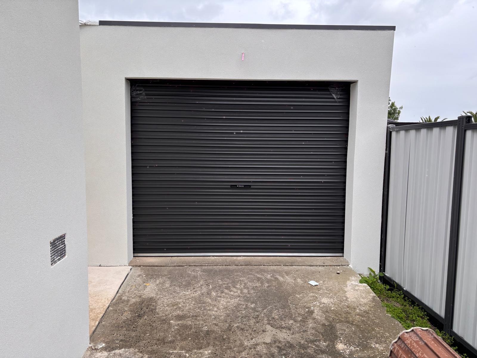Black roller garage door in a white rendered opening